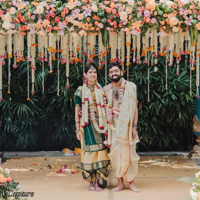 A classic portrait of the couple at their South Indian wedding mandap. The structure is beautifully decorated with colorful flowers and traditional elements, creating a perfect frame for this timeless photograph.