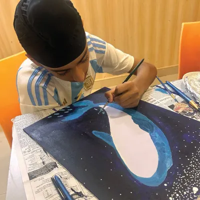 Concentration is key. This young artist is meticulously adding the final touches to his deep-sea whale painting, learning about fine brush control and detail work.