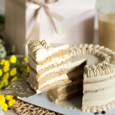 When cold coffee meets cake. This is our Vanilla Latte Cake, featuring moist vanilla cake infused with rich coffee and layered with a homemade coffee mascarpone frosting. A slice is being lifted to show the beautiful layers inside.