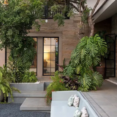In this Alibaug home, I designed a sunken outdoor lounge surrounded by lush greenery. The built-in seating is nestled amongst large Monstera plants and ferns, creating a private, cozy nook that feels completely immersed in nature.