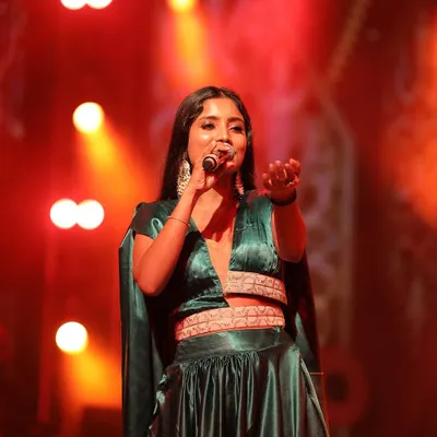 Singer Divya Ramachandra looks stunning on stage in this custom-designed emerald green Indo-western outfit. The crop top with an attached cape and the flowing satin skirt are designed for performance and movement.