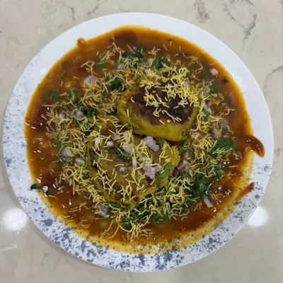 Our Ragda Pattice is a complete meal in itself. It features soft potato patties (pattice) stuffed with a delicious filling, served in a flavorful white pea curry (ragda) and topped with sev and chopped onions.