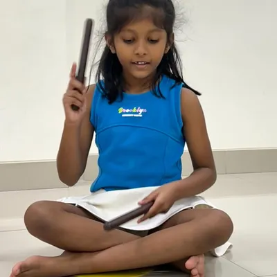 A student uses claves to tap out a rhythm shown on a flashcard. This exercise directly connects visual notation with auditory and kinesthetic learning, reinforcing the concept of rhythm in a multi-sensory way.