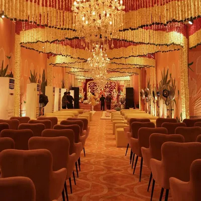 A grand hall prepared for a traditional ceremony, with the ceiling covered in thousands of cascading marigold and tuberose garlands. The opulent crystal chandeliers add a touch of modern luxury to the sacred space.