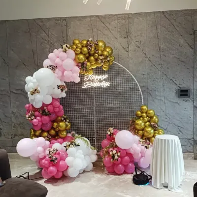 A beautiful circular mesh backdrop decorated with a pink, white, and gold balloon garland. This chic setup includes a 'Happy Birthday' neon sign and is perfect for photos.