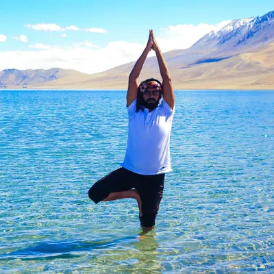Embodying balance with a Vrikshasana (Tree Pose) in the crystal-clear waters of Pangong Lake. Practicing yoga in nature, surrounded by the majestic Himalayas, is a truly spiritual experience.