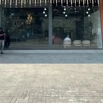 The exterior of a commercial establishment featuring a full-glass facade and a wide, paved entrance area. This design creates an open and inviting feel, encouraging foot traffic and connecting the interior with the streetscape.