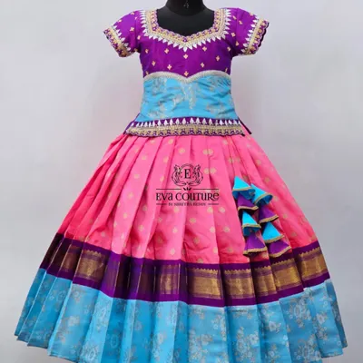 A colorful pattu pavadai with a multi-layered skirt in pink and blue. The purple peplum top has delicate embroidery, tying the colors together.