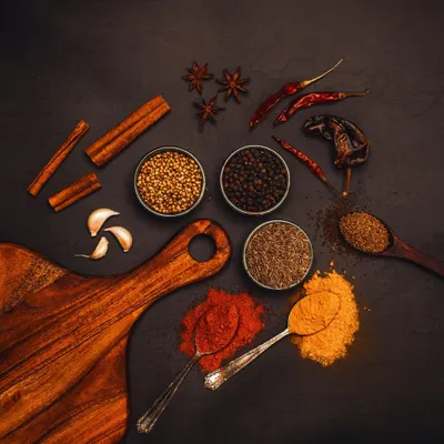 An assortment of whole and powdered Indian spices on a dark slate background. This top-down, moody shot highlights the vibrant colors and textures of the spices, creating a rich and aromatic scene.