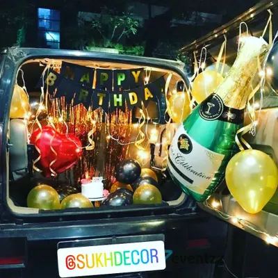 A classic car boot birthday surprise, perfect for a celebration anywhere. This setup includes a 'Happy Birthday' banner, a shiny backdrop, gold and black balloons, and a large champagne foil balloon.