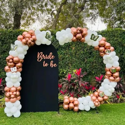 An elegant outdoor 'Bride to be' setup. This design uses a circular balloon arch in rose gold and white against a black arched backdrop, perfect for a garden party or daytime event.