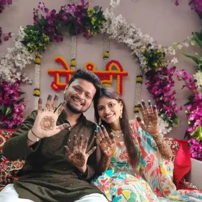 A happy couple proudly showing their mehandi designs during their celebration. The groom has a simple mandala, while the bride has intricate patterns on her palms.