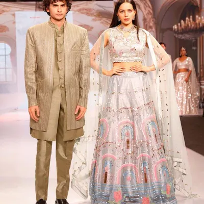 A high-fashion runway look you can rent. This coordinated set features a modern pastel lehenga with a cape and a sleek, matching Indo-western for him.