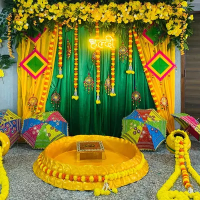 A complete Haldi ceremony setup with a traditional 'urli' for the rituals. The backdrop features yellow and green drapes, marigold garlands, and Rajasthani umbrellas.