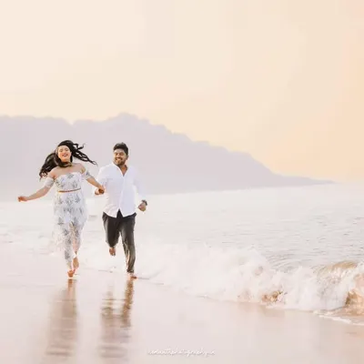 A couple runs joyfully along the shoreline at sunrise, hand in hand. This candid action shot captures their carefree energy against a soft, golden-hour backdrop.