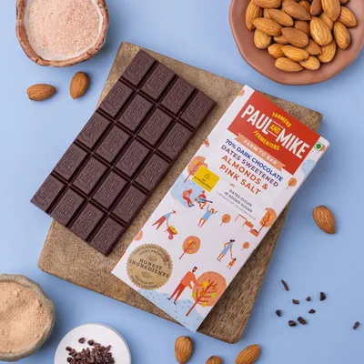A Paul & Mike dark chocolate bar with almonds and pink salt, styled on a wooden board to give it a rustic, farm-to-bar feel.