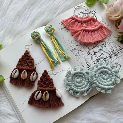 A showcase of the diverse earring styles I create by hand. This collection features brown tassel earrings with cowrie shells, two-tone knot and tassel earrings, soft pink fan-shaped fringe earrings, and light blue spiral designs, all laid out to show the intricate details of my boho jewelry.