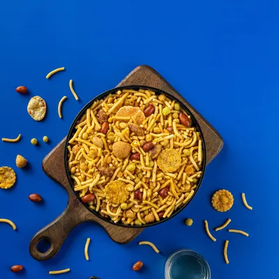 A flat-lay photograph of a savory Indian snack mix for Sartaj Sweets & Namkeen. The bold blue background makes the product pop, a technique I use for effective packaging design.