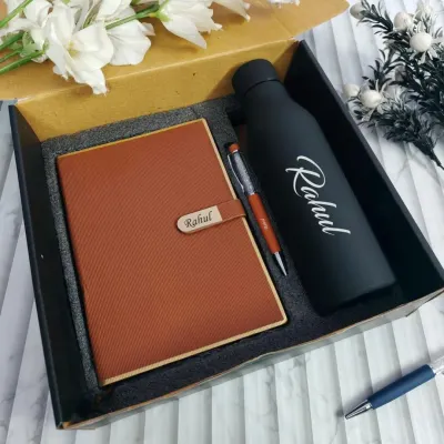 A classic personalized gift set, perfect for any professional. This combo includes a tan faux-leather diary with a name-engraved clasp, a matching pen, and a matte black temperature bottle with the name "Rahul" printed on it.