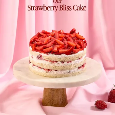My Strawberry Bliss Cake, showcased on a marble stand. This naked-style cake features layers of fluffy vanilla sponge, fresh cream, and is generously topped with chopped strawberries.