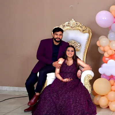 The happy couple seated on a classic white and gold throne chair, ready to celebrate their upcoming arrival in front of our custom decor.