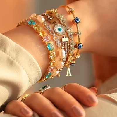 A maximalist wrist stack that is giving everything. This look combines colourful gems, pearls, initial charms, and evil eye bangles for a truly stunning statement.
