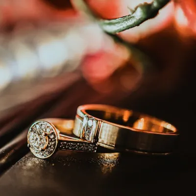 A stunning macro shot of the wedding rings, resting on a dark surface with a warm, colorful bokeh background. This artistic photo turns the symbol of your union into a beautiful work of art.