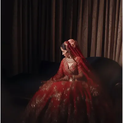 A bride in her full glory. This portrait of Anshika in her stunning red lehenga uses dramatic, low-key lighting to create a sense of timeless elegance and quiet contemplation.