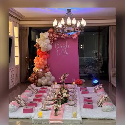 A stunning "Bride to Be" setup for an intimate bridal shower. This luxurious floor seating arrangement features a vibrant pink backdrop, a beautiful organic balloon arch, elegant floral runners, and personalized gift boxes for each guest.