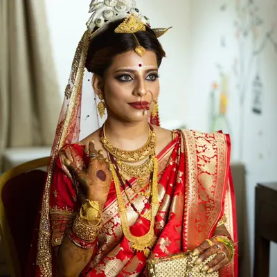 A stunning portrait of a Bengali bride in her traditional red Benarasi saree, adorned with a 'mukut' and intricate gold jewelry.