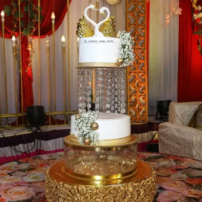 A beautiful three-tier engagement cake featuring crystal chandeliers and elegant swan toppers, set up at a grand venue. We show you how to assemble these showstoppers on-site.