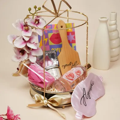 This birthday hamper for her is a dream in pink. It's curated with a personalized eye mask and hairbrush, a bottle of rosé wine, and other pampering goodies in a beautiful gold and black cage basket.