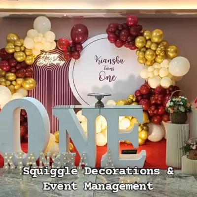A sweet first birthday setup with a large marquee 'ONE', a custom circular backdrop, and a red and gold balloon garland.