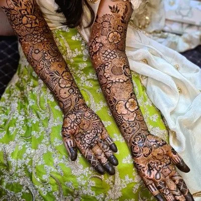 A complete view of a full bridal henna application, showcasing dense floral and geometric patterns. Both arms are covered in unique, complementary designs, a specialty for my bridal clients.