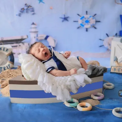 Ahoy, little sailor! This newborn is captured mid-yawn in a boat-shaped prop, surrounded by a complete nautical set with anchors, lifebuoys, and a lighthouse.