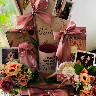 A closer look at the top tier of the personalized wedding hamper, showcasing a custom 'Here Comes the Bride' box, a fun mug, and photos of the bride with her friends, all adorned with beautiful silk flowers.