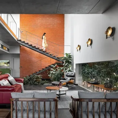 A sleek metal staircase ascends alongside a warm, exposed brick wall in the double-height living area. This feature connects the home's two levels while acting as a backdrop to the indoor courtyard, blending industrial and natural elements.