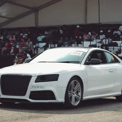 A white Audi A5 coupe at the starting line, with the packed grandstand in the background. This is where performance meets a passionate audience.