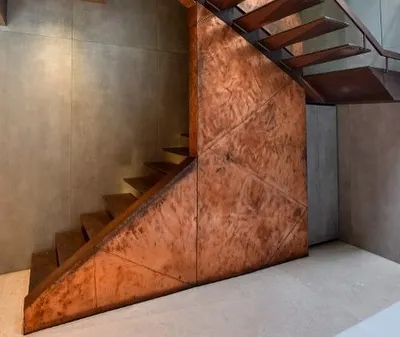 This copper and metal staircase at a Sainik Farms residence is designed as a sculptural element. The cantilevered treads create a sense of lightness, while the textured copper cladding adds warmth and intensity, heightening the sense of ascent.