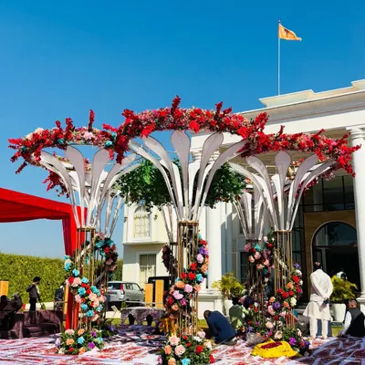 A spectacular modern mandap with a unique, multi-tiered structure, adorned with a mix of red and colorful flowers, set against a grand building.