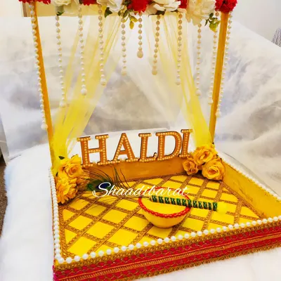 This is one of my most loved Haldi platter designs. It features a beautiful canopy decorated with red and white flowers and pearl strings, over a quilted yellow tray with a matching bowl for the haldi paste.