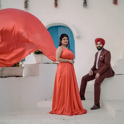 A dramatic shot at our Santorini set, featuring a woman in a flowing red gown. The contrast against the white architecture creates a powerful and visually striking pre-wedding photograph.