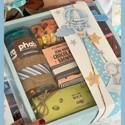 A closer look at our hot air balloon and elephant themed first birthday hamper. It’s filled with goodies like a granola jar, chocolate brownies, and pistachio roca, all wrapped with a custom sleeve.