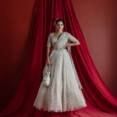 A full-length view of the magnificent ivory bridal lehenga, complete with a matching potli bag. The entire ensemble, from the detailed skirt to the draped dupatta, is designed to create a cohesive and breathtaking bridal statement against a dramatic red backdrop.