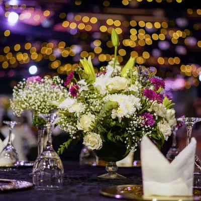 A close-up of a lush floral centerpiece, with a beautiful bokeh effect from the event lighting in the background. We use a mix of flowers like lilies, roses, and chrysanthemums to create texture and depth in our arrangements.