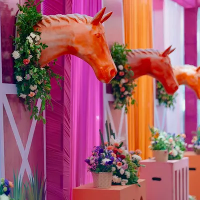 A close-up of the equestrian-themed Haldi decor, where horse-head sculptures emerge from vibrant pink stable-like walls, adorned with fresh flowers.