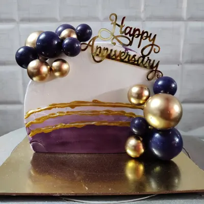 A modern and stylish anniversary cake. This unique design features a half-cake shape with purple and gold spheres and abstract gold lines.