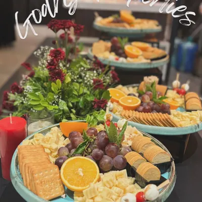 A trio of gourmet cheese platters prepared for a Godrej Properties event. Each platter is artfully arranged with a selection of cheeses, crackers, fresh grapes, and orange slices, complemented by a beautiful floral centerpiece.