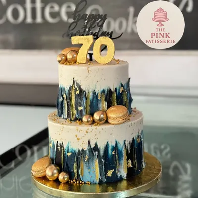 A striking two-tiered cake for a 70th birthday. This modern design features a brushed blue and gold effect, accented with gold macarons, spheres, and a bold "70" topper.