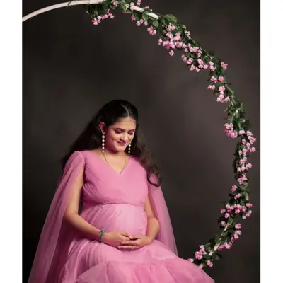 A serene solo portrait of the mother-to-be in our pink ruffle gown. The floral ring prop frames the shot beautifully against a simple dark backdrop.